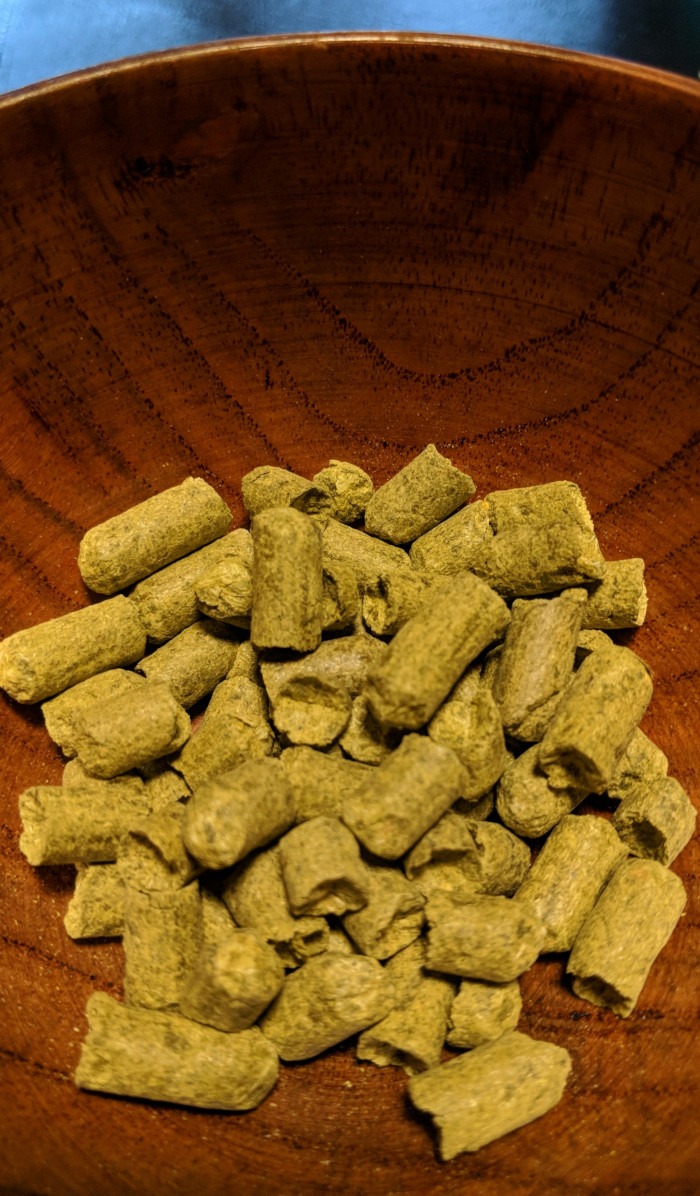 A small collection of dried, green Williamette hop pellets in a small, brown bamboo bowl
