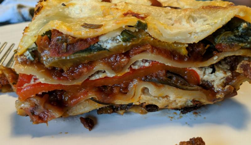 A slice of vegan lasagne, showing the layers of pasta and fillings (baked peppers, courgettes, spinach, bechamel and ragu)