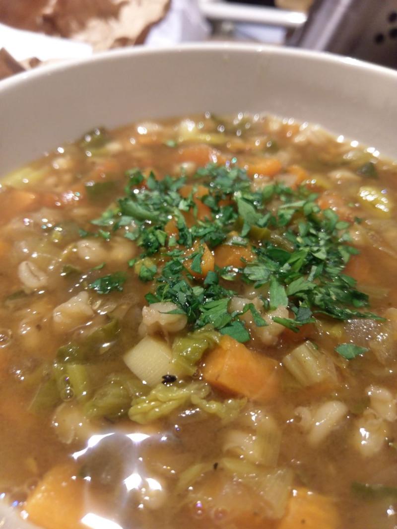 close up shot of a brownish soup with various root vegetables, barley, spinach and some fresh parsley