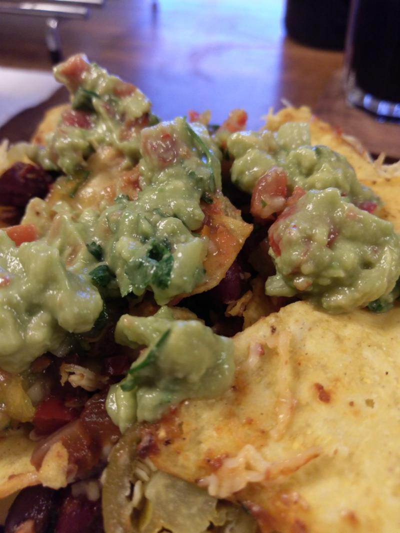 close up of the nachos, salsa and guacamole from previous photos on a small side plate.