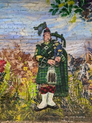 a mural of a bagpiper dressed in Highland wear and a green kilt