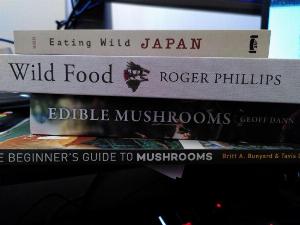 上から順に、「Eating Wild in Japan」、「Wild Food」、「Edible Mushrooms」、「A Beginner's Guide Mushrooms」というタイトルの本の束。日本の野生を食べる」、「野生の食べ物」、「食べられるキノコ」、「キノコの初心者ガイド」。