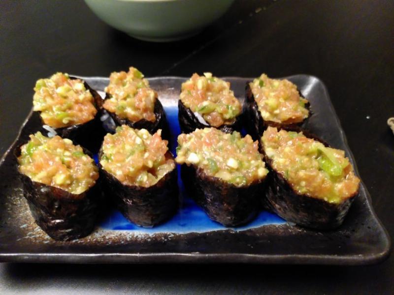 A blue plate on a black table on top of which are 8 Gunkan (boat-shaped) sushi the filling is tomato, avocado and spring onion.