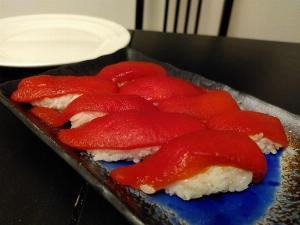 A blue plate on a black table.  on the plate are 8 nigiri sushi, with a bright red, marinated red pepper topping.