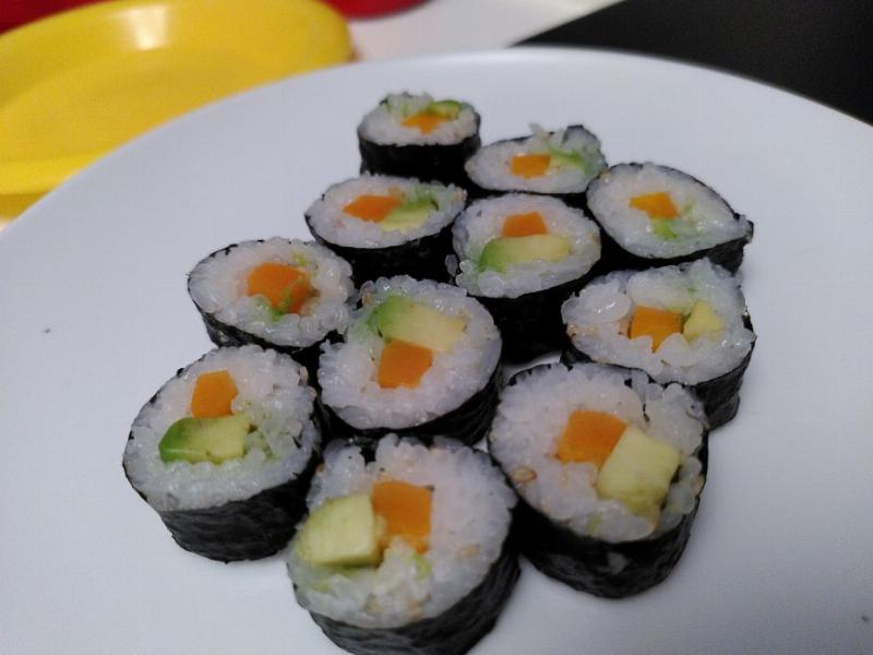 A small white plate with a number of small maki sushi for our daughter.  filling is carrot and avocado.