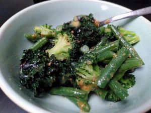 A white bowl holds some greens in miso sauce: kalettes, brocolli and runner beans.