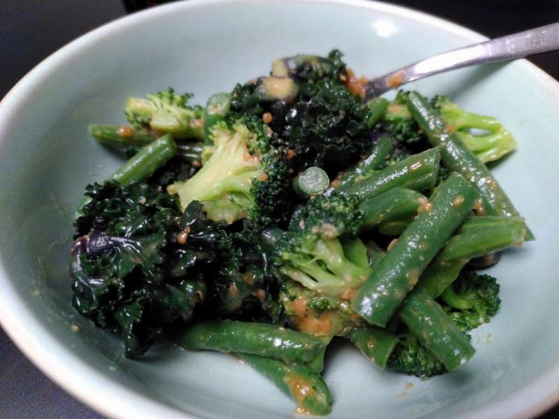 A white bowl holds some greens in miso sauce: kalettes, brocolli and runner beans.
