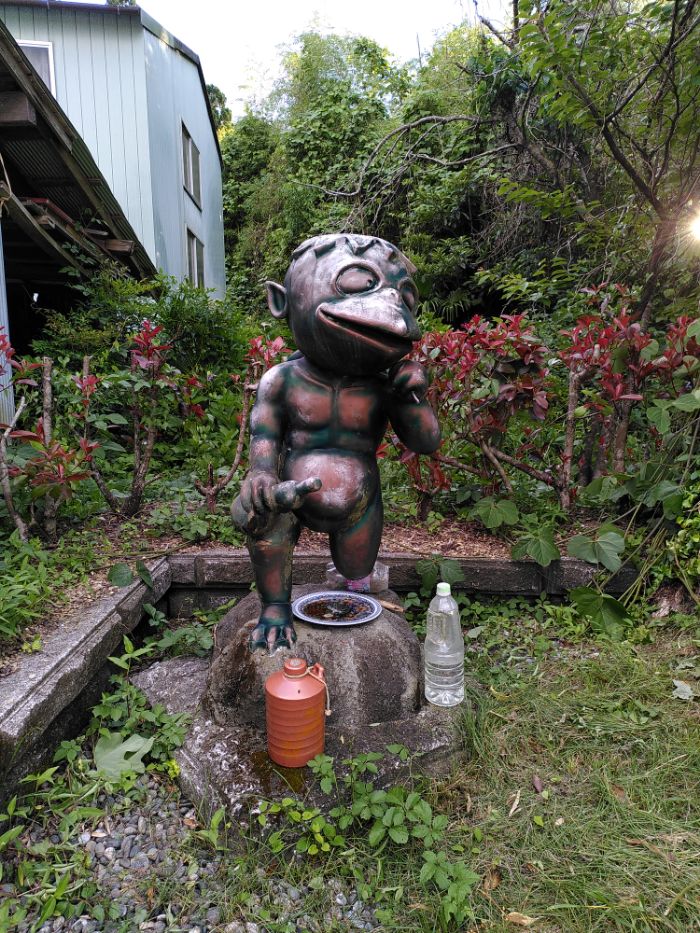 a bronze-ish statue of the folklore character Kappa, surrounded by bottles of sake seemingly.