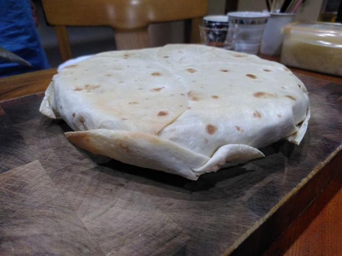 A tortilla wrapped parcel sits atop a dark brown wooden chopping board.