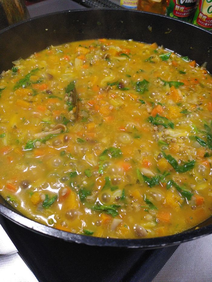 A black pot holds an oranges hewed stew of pumpkin, barley, carrots, onions, celery, parsley, celery leaf, cabbage and spinach.