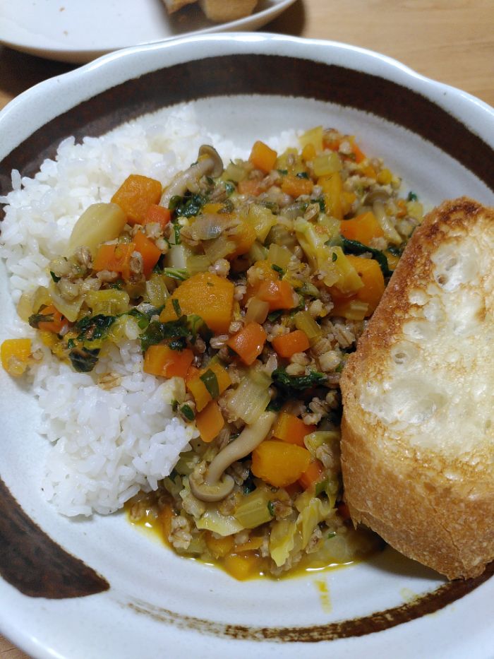 A white bowl with brown rim holds white rice, the pumpkin and barley stew and some toasted French bread.