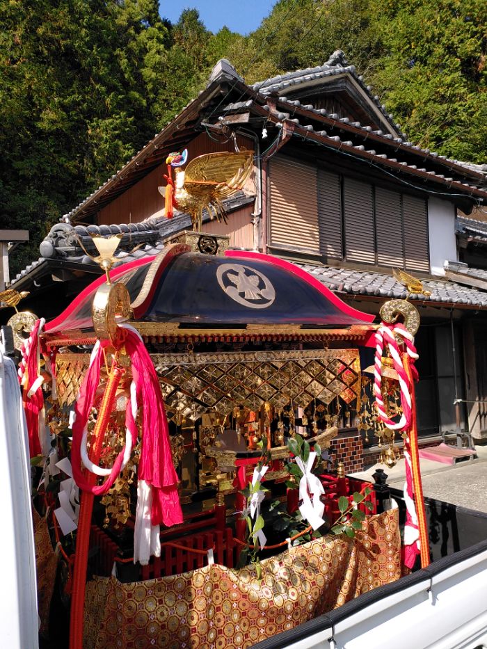 the mobile shrine, very old, is a shiny structure of gold black and red, there is a gold bird on top and various red torii gates around it.