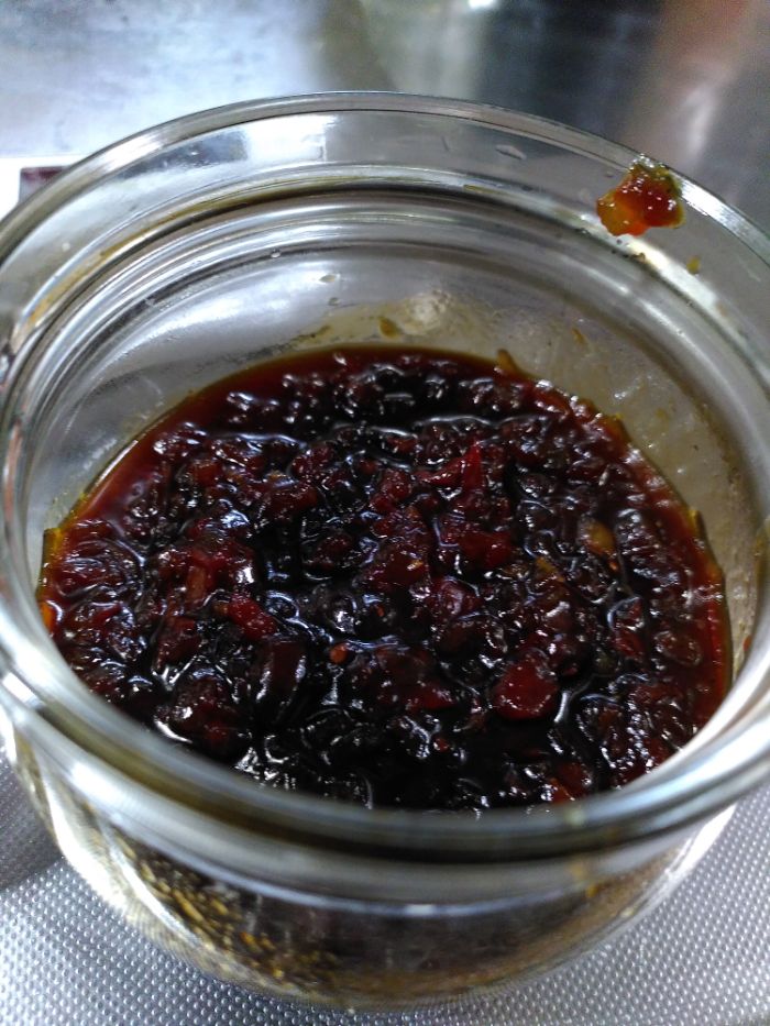 a glass jar with a dark red tomato relish inside