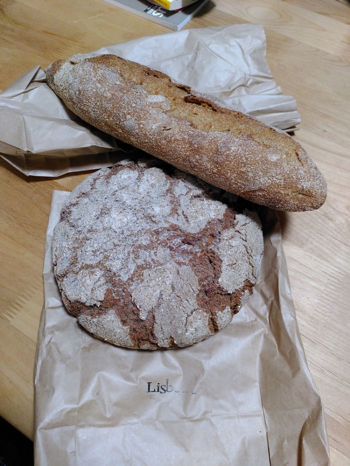 a wholewheat and rye loaf and a brown rice flour and rye broa on the brown bag from the bakery.