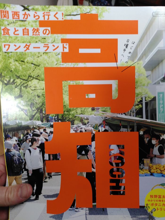 the cover of a magazine with the prefecture name in bold orange Japanese character, the cover image is a market scene.