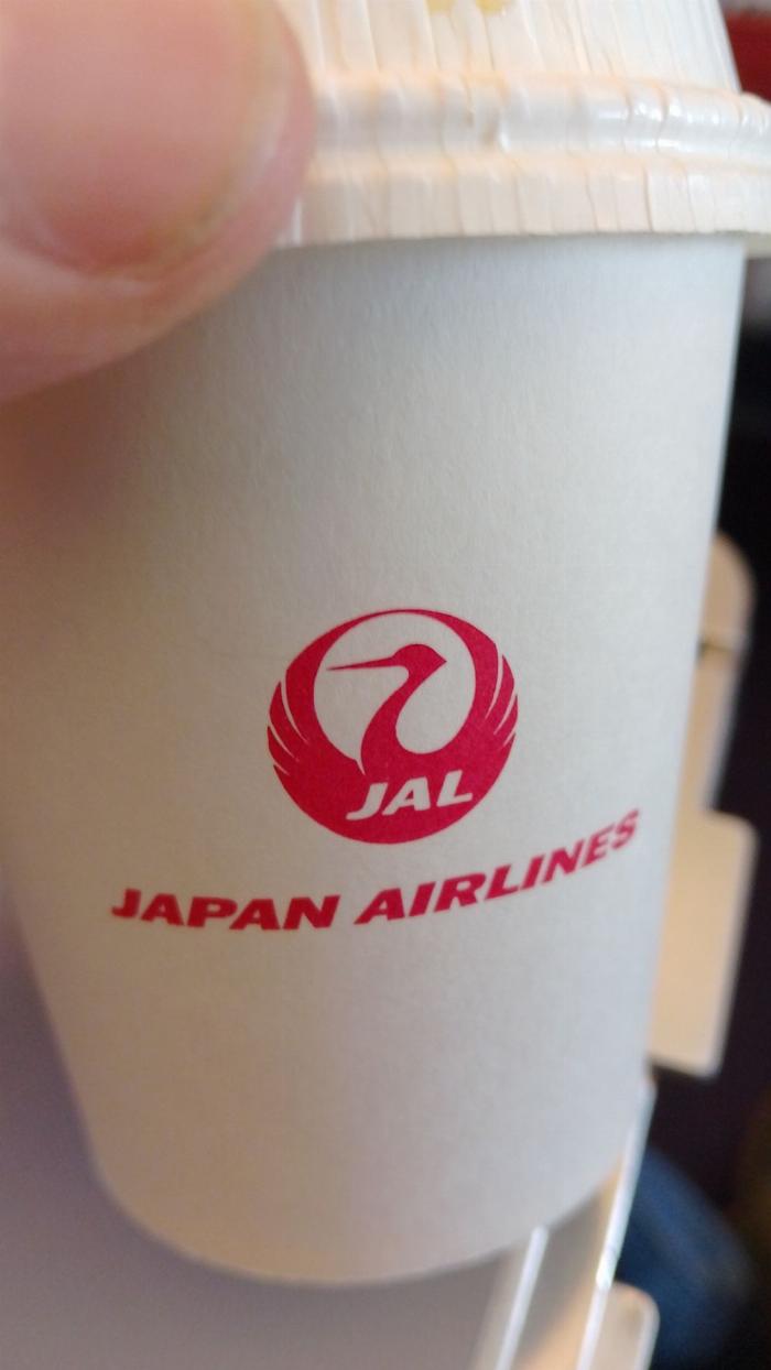 Kinda boring shot of a small paper coffee cup with the Japan Airlines logo on it.