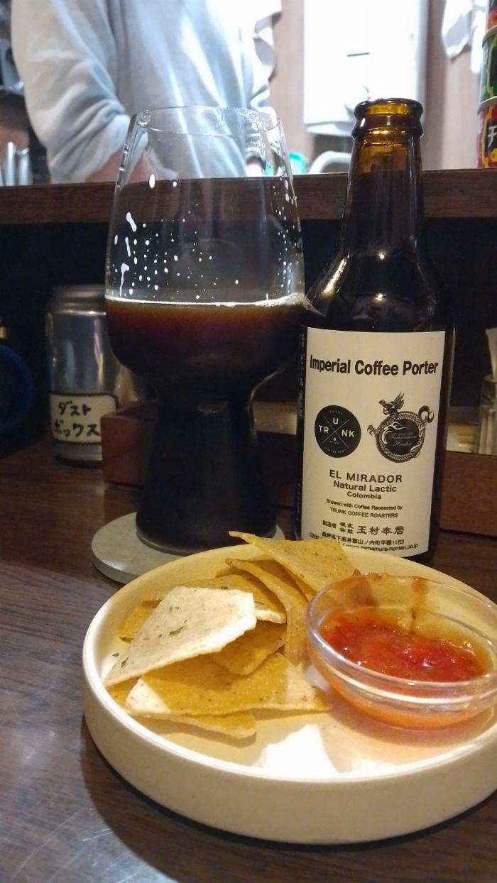 a plate of nachos with salsa behind which is a pint glass containing imperial coffee porter along side its companion bottle.