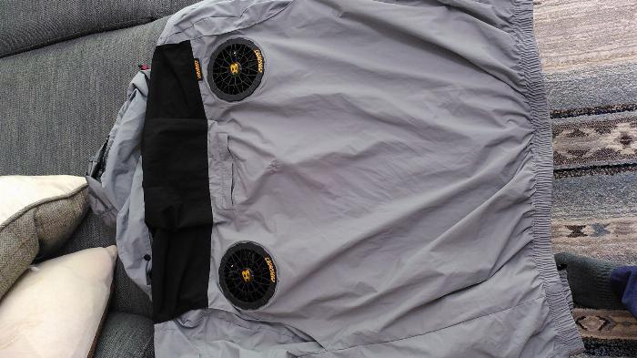 A light grey short sleeved jacket with hood lies on a grey sofa, there are two black fans just under where the wearer's shoulder blades will be.
