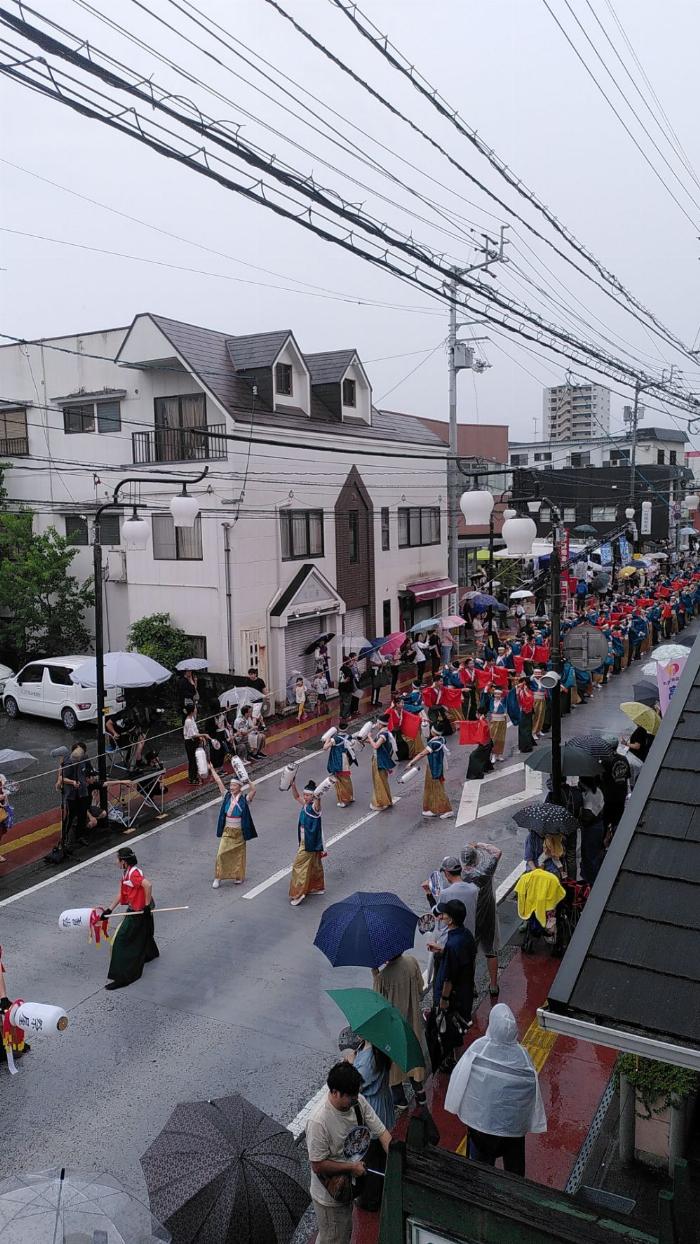 view of a rainy Japanese city street view with an approaching group of dancers in colourful uniforms 