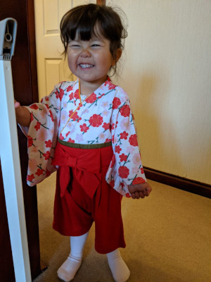 Photo of a young girl in a furisode, red on bottom, white with red flowers on top, sporting a cheeky grin